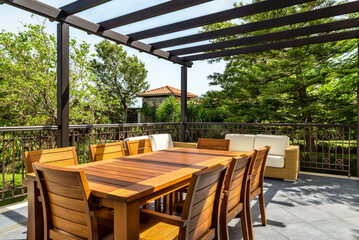 Wooden outdoor table with matching chairs on terrace surrounded by lush greenery. Natural setting creates cozy and inviting atmosphere, perfect for outdoor dining or relaxing amidst vibrant plants.