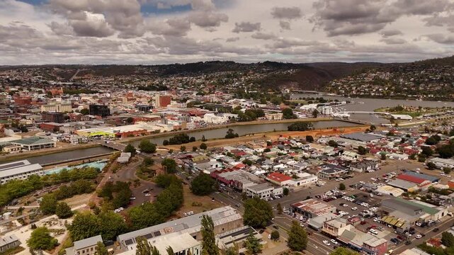 Aerial flyover Launceston City with North Esk River during cloudy day in Tasmania. Cars crossing river over bridge. Drone wide shot.