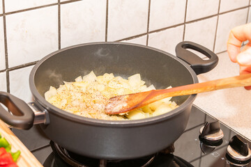 A cooking pot on gas fire with onions, wooden cutting board with freshly cut green, red, yellow paprikas. The gas fire is on. Healthy food cooking, home made healthy dinner. Fresh vegetables.