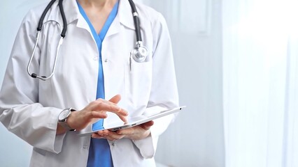 Doctor woman is using digital tablet in clinic. Healthcare professional with a stethoscope operating a touch screen tablet computer while standing straight. Medicine concept