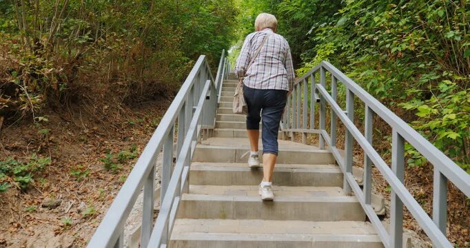 An elderly woman climbs up a long staircase in a park.