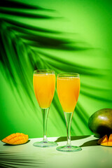 Summer alcoholic cocktail with champagne, mango juice, syrup and ice, green background, hard light