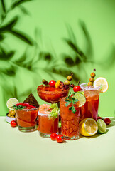 Tomato juice and vodka alcoholic cocktails with hot sauce, salt, pepper, olives and celery. Bloody mary cocktail party. Green  background, hard light
