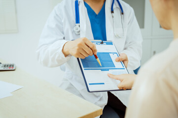 A male Asian pediatrician in a white lab coat sits at his desk, warmly greeting a middle-aged pregnant woman for a prenatal consultation, offering care and support in a clinical setting.