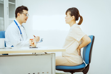 Fototapeta premium A male Asian pediatrician in a white lab coat sits at his desk, warmly greeting a middle-aged pregnant woman for a prenatal consultation, offering care and support in a clinical setting.