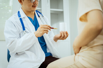 A male Asian pediatrician in a white lab coat sits at his desk, warmly greeting a middle-aged pregnant woman for a prenatal consultation, offering care and support in a clinical setting.