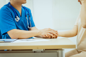 A male Asian pediatrician in white lab coat gently holds hand of middle-aged pregnant woman, encouragement and support during prenatal care consultation focused on maternal and child health.