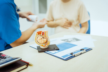A male Asian pediatrician in a white lab coat conducts a prenatal checkup for a middle-aged...