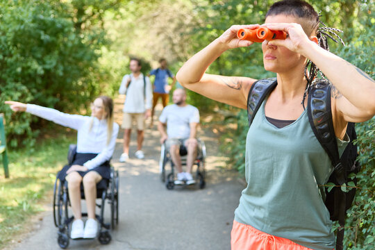 Group of friends on outdoor adventure, woman using binoculars, inclusion of persons with disabilities