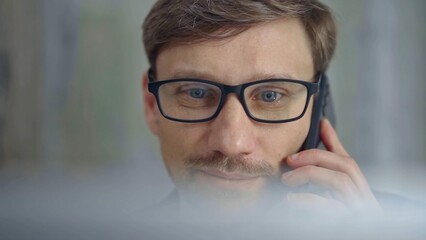 Businessman with glasses speaking on the phone, partially obscured by blurred laptop. Front view and close up portrait