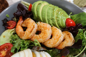 close up of healthy salad with avocado, prawns, shrimps, boiled egg, cherry tomato, vegetables in a blue bowl