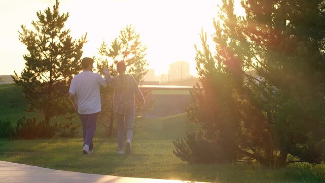 Young couple is walking in the park as the sun is setting. They're just messing around, holding hands and having fun.