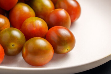 Freshly picked kumato cherry tomatoes on a ceramic plate close up. Vegetable organic ingredients. Top view. 