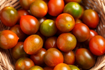 Fresh raw small kumato cherry tomatoes in a rattan bowl close up. Top view