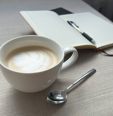 A cup of coffee and a white notepad on the table in the morning