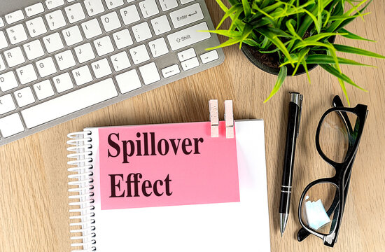 Spillover effect concept on a notebook with a keyboard, glasses, pen, and plant on a wooden desk