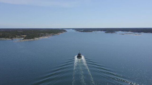 Small tugboat making way ahead in Finnish archipelago fairway. High altitude aerial chasing view.