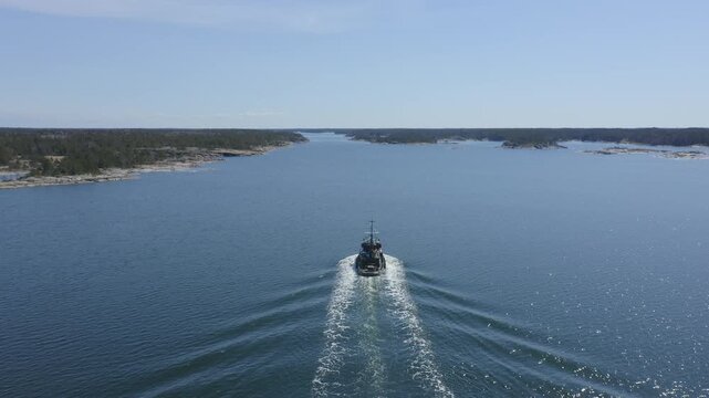 Small tugboat making way ahead in Finnish archipelago fairway. Descending aerial chasing view.