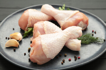 Raw chicken drumsticks with spices on plate on black wooden background.