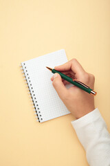Woman hands hold opened notebook pages with pen on beige background. Top view