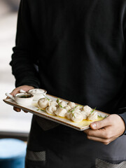 handsome man in a black sweater is holding delicious juicy dumplings with fragrant herbs and cracklings, served with buttery sauce and sour cream in a beautiful dish on a wooden table