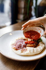 handsome man is eating delicious dish with juicy chicken, fresh vegetables, and crispy lavash, served with adjika sauce and fragrant herbs on a beautiful white plate on a wooden table 