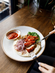 handsome man is eating delicious dish with juicy chicken, fresh vegetables, and crispy lavash, served with adjika sauce and fragrant herbs on a beautiful white plate on a wooden table 