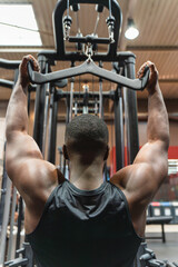 Fototapeta premium Muscular black man training back in the gym with pulleys