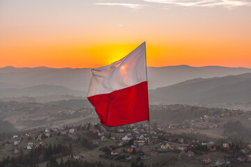 Biało-czerwona flaga Polski na tle zachodzącego słońca w górach - Ochodzita, Koniaków