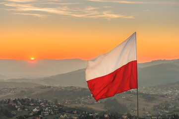 Biało-czerwona flaga Polski na tle zachodzącego słońca w górach - Ochodzita, Koniaków