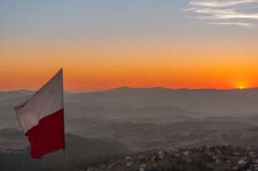 Biało-czerwona flaga Polski na tle zachodzącego słońca w górach - Ochodzita, Koniaków