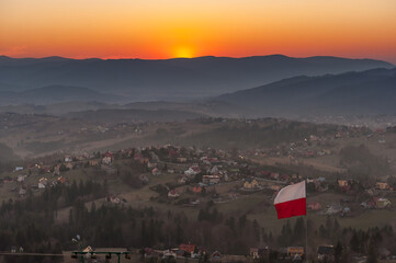 Biało-czerwona flaga Polski na tle zachodzącego słońca w górach - Ochodzita, Koniaków