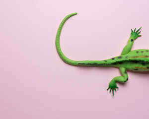 Tail of green lizard toy on pastel pink background. Minimal art concept.