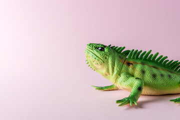Green lizard toy on pastel pink background. Minimal art concept.
