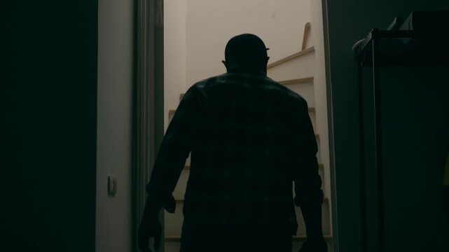 Slow motion of a man in a striped shirt, cap and holding a pistol walking up stairs. Concept of burglary, trespassing, murder.