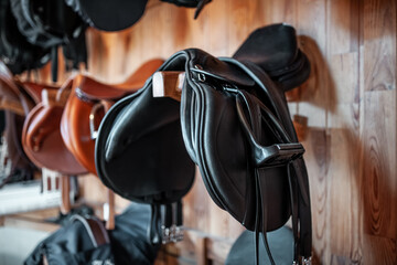 black leather saddle hanging on wooden wall at stable or barn, professional equestrian horse riding...