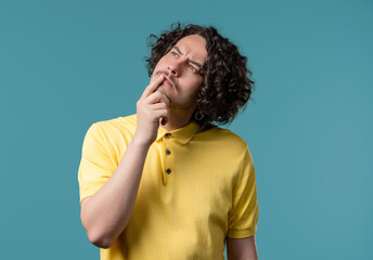 Curious thinking around curly man on blue. Confused student guy finding answer