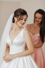 Fototapeta premium A bride is getting ready for her wedding with her bridesmaid. The bride is wearing a white dress and a veil. Scene is happy and celebratory