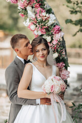 A bride and groom are posing for a picture in front of a pink arch. The bride is holding a bouquet...
