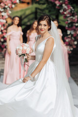 Naklejka premium A bride is wearing a white dress and holding a bouquet of pink flowers. She is standing on a white carpet in front of a pink archway
