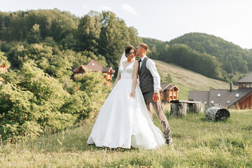 Fototapeta premium A bride and groom are kissing in a field with a view of a house in the background. Scene is romantic and happy