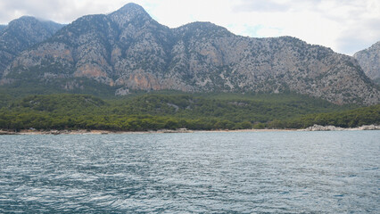 Landscape with crystal clear blue water and rocky shore in Turkey, Steep mountainside covered with tropical vegetation,