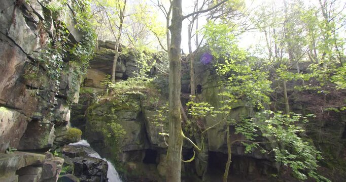 Wide tilting up shot of the Lumsdale waterfalls with rocks and trees in foreground at Lumsdale, Matlock