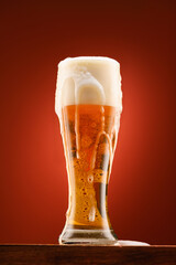 a glass of beer, a wooden stand, a red background, a close-up view of the object, beer bubbles and foam