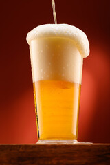 pouring beer into glass, wooden stand, red background, close-up view of object, beer foams and bubbles