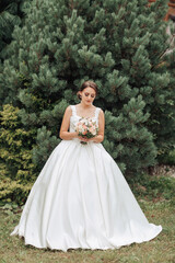 Fototapeta premium A woman in a white dress is standing in front of a tree, holding a bouquet of flowers