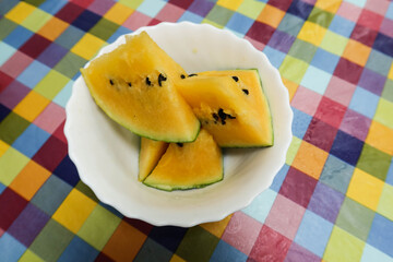 close up of yellow water melon sliced and cut to pieces on a plate with colourful table cloth