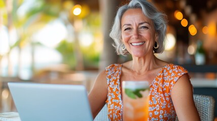 A content gray-haired woman with a laptop and a refreshing drink sits at a beach venue, enjoying the blend of work and leisure, displaying a serene and balanced life.