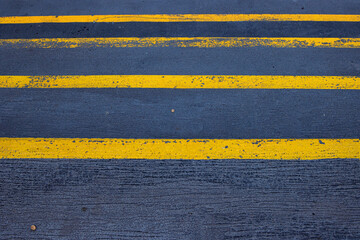 Fototapeta premium Closeup of a textured asphalt road with weathered yellow stripes on a rough gray pavement, great for use in street photography, urban design, or traffic-related visuals. Copy space 