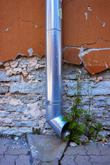 Galvanized metal downspout dreainpipe against an old weathered stone and cracked stucco wall. ...